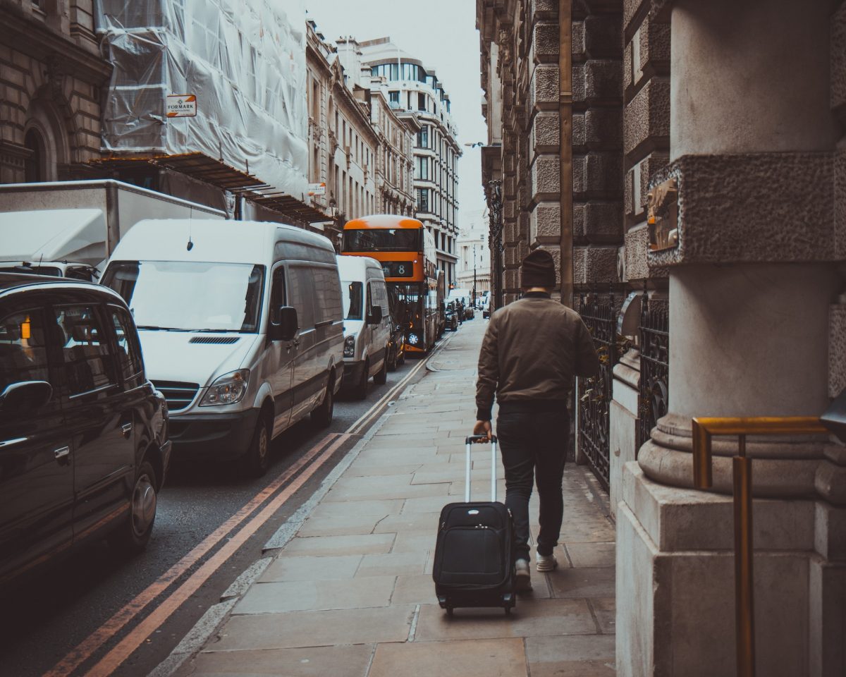 A person walking down the sidewalk carrying a rolling luggage.