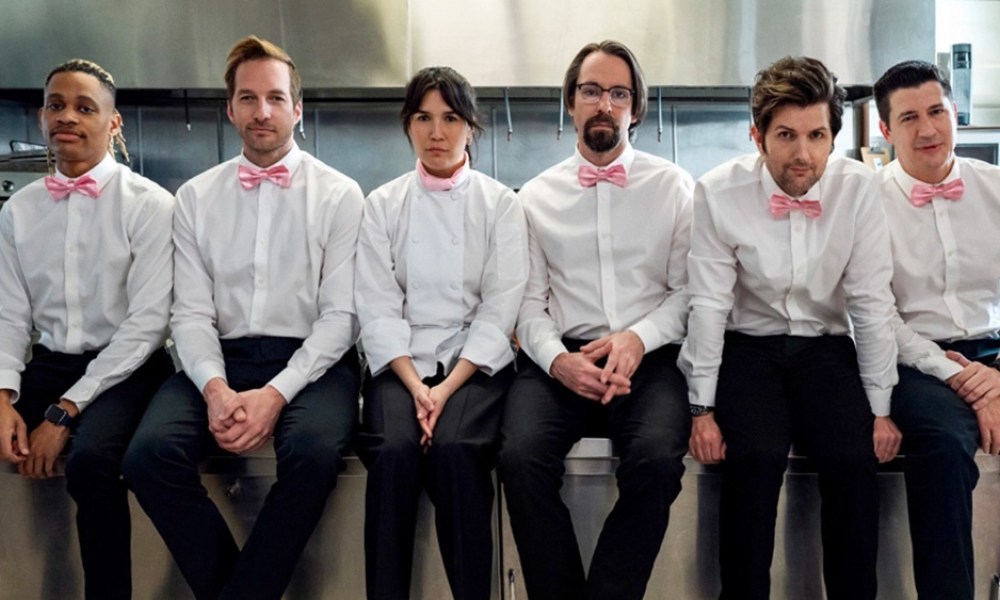 The cast of Party Down in uniform sitting on a counter.