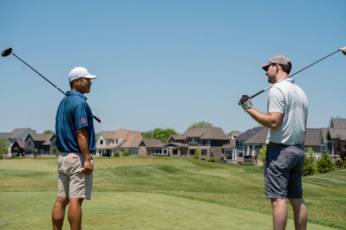 Two people looking at each other while holding their golf clubs over their shoulders.