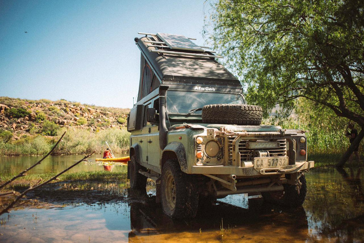 Alu-Cab Icarus Roof Conversion package on a Land Rover Defender parked next to a river.