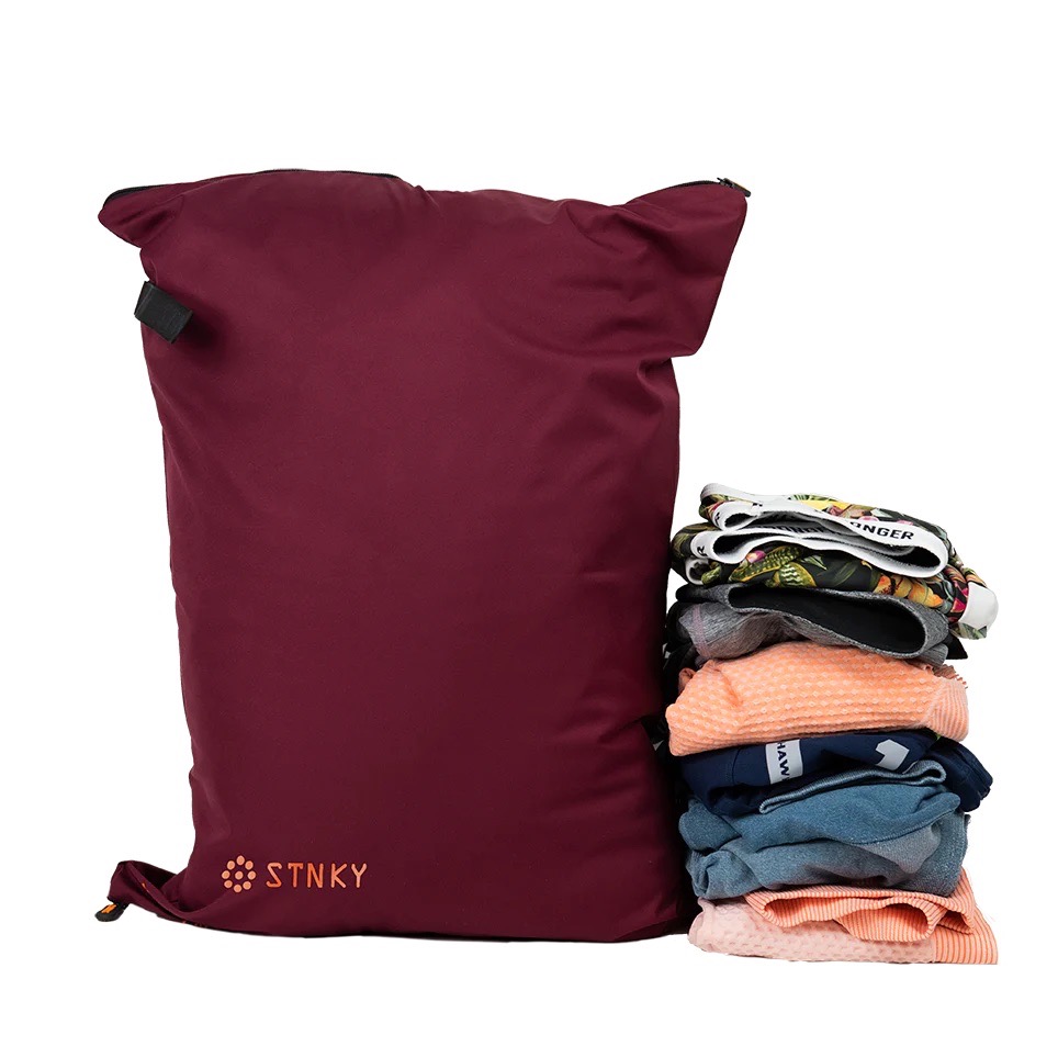 A STNKY washable laundry bag with a stack of laundry beside it