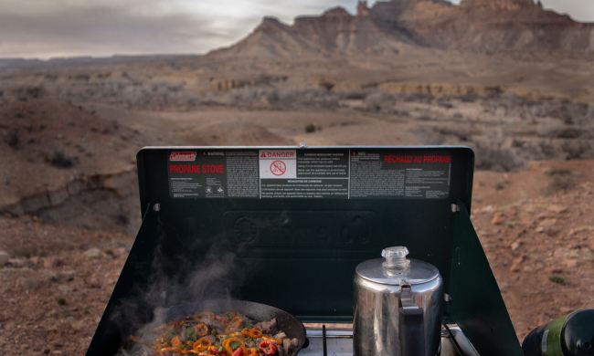 A camp stove cooking food with a desert landscape blurred in the background