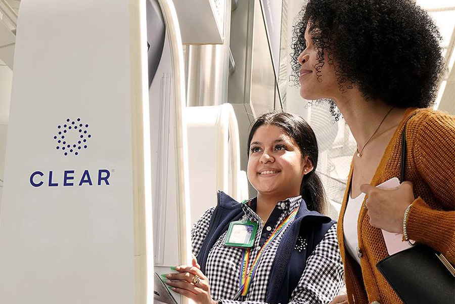 CLEAR program representative helping a traveler at an airport kiosk.