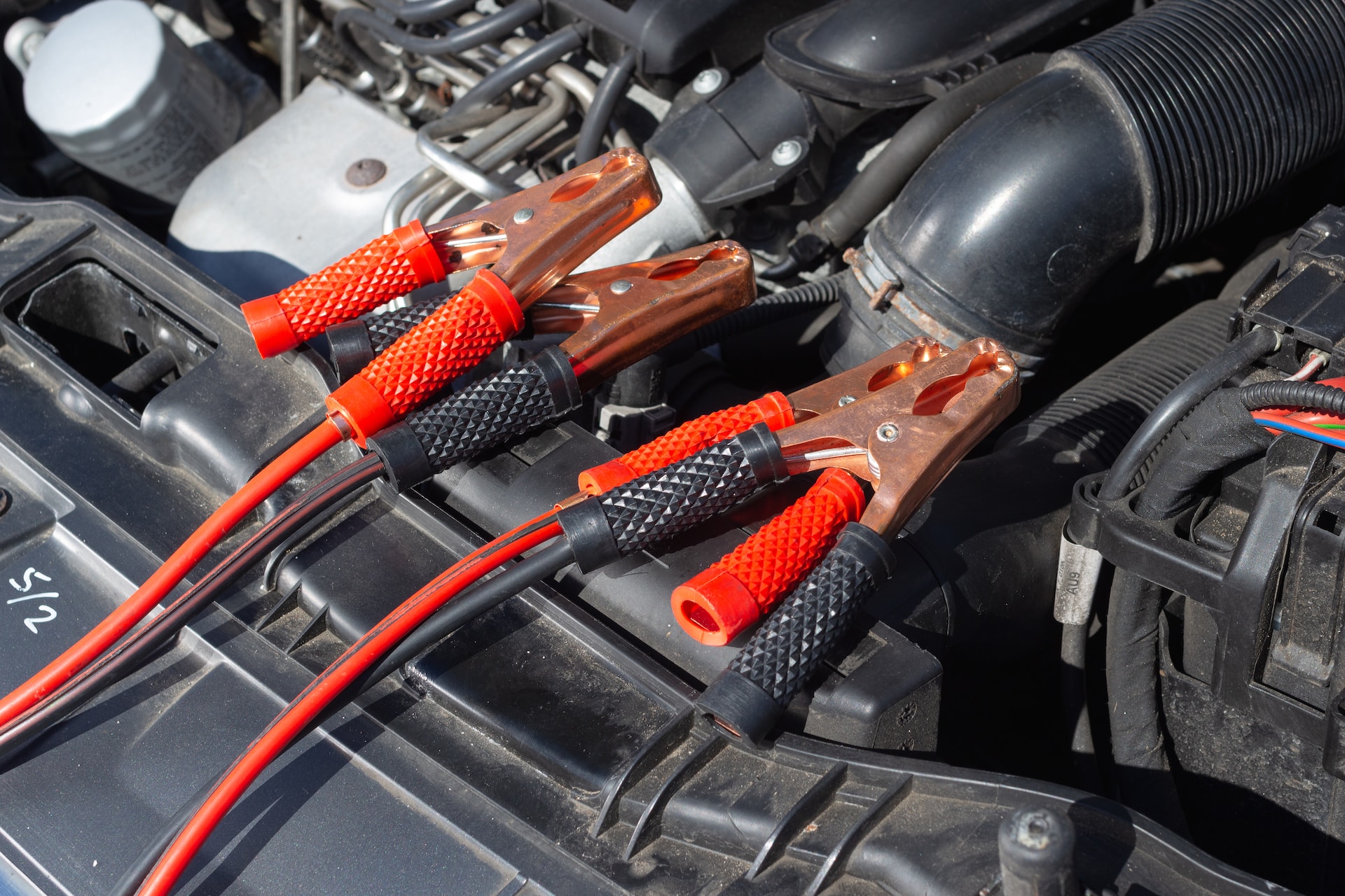 Battery jumper cables lying underneath a car's open hood.