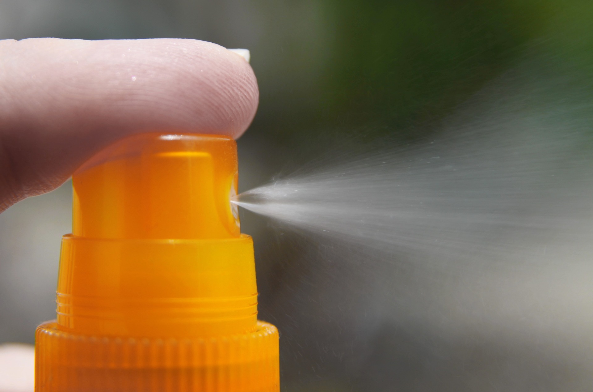 Closeup of a finger on the pump of a sunscreen spray bottle.