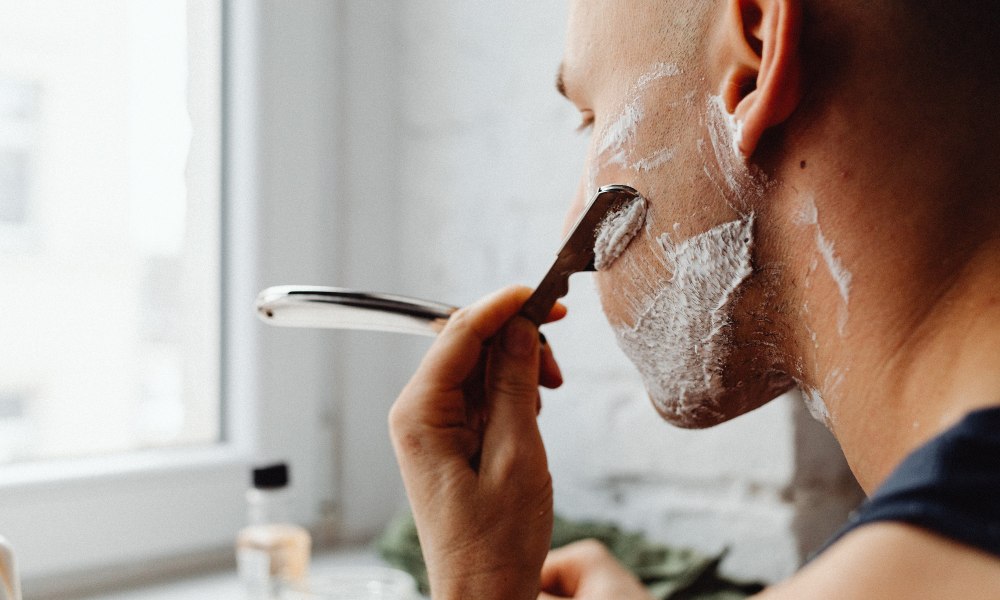 Bald man shaving face over sink