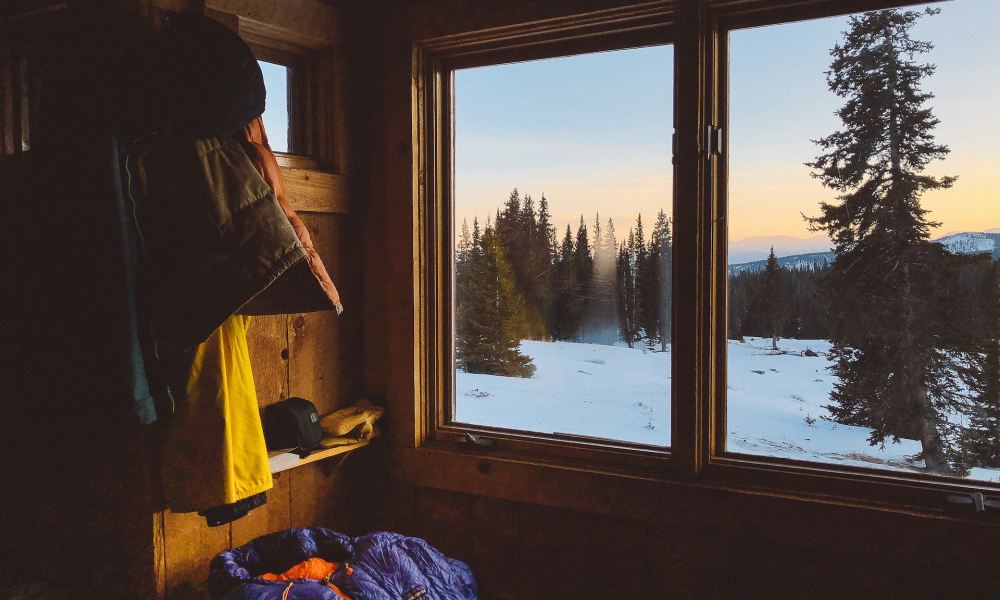 A sleeping bag inside a camping hut with snow on the ground outside.