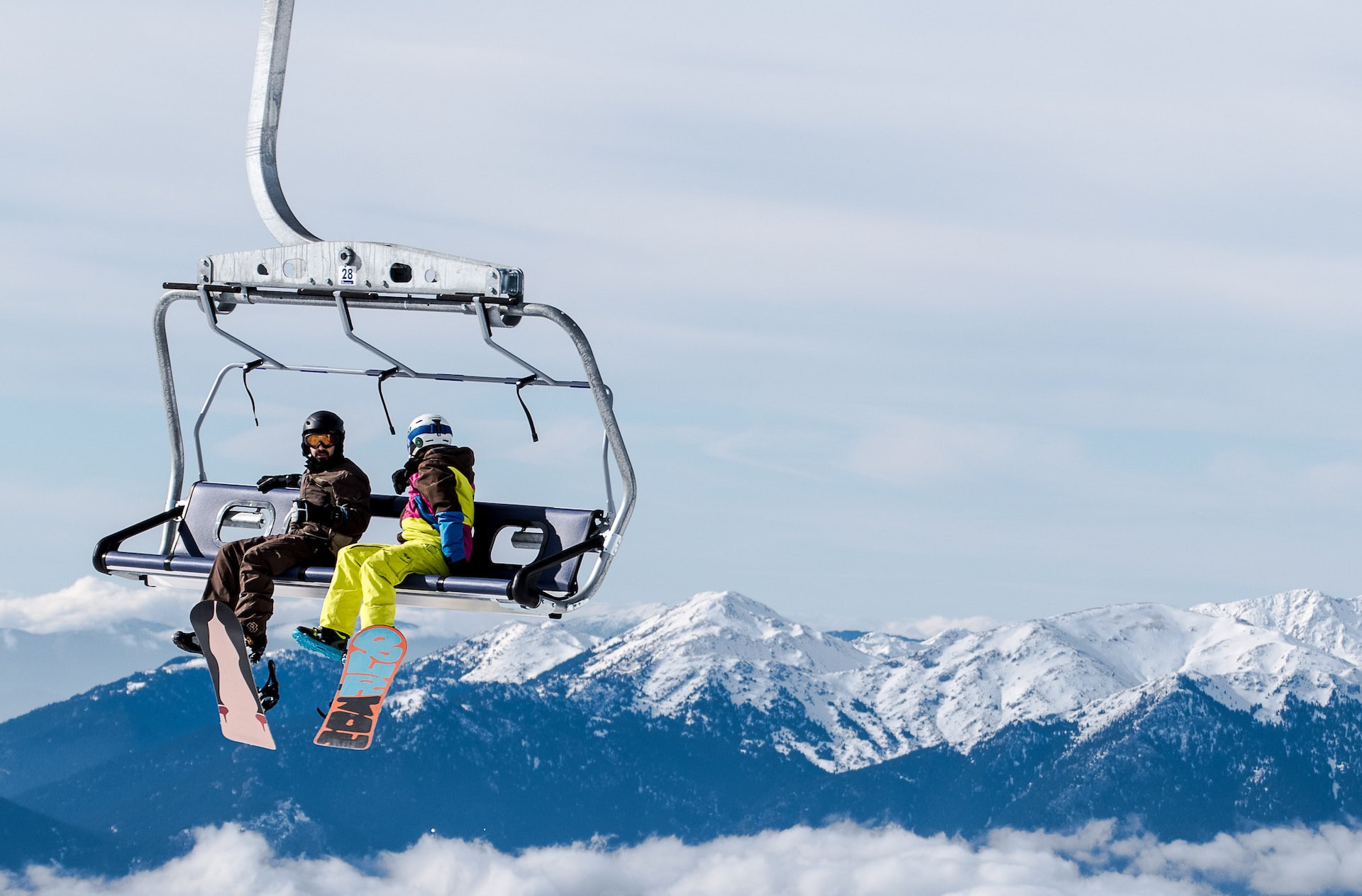 Two snowboarders on a ski lift with mountains behind them.