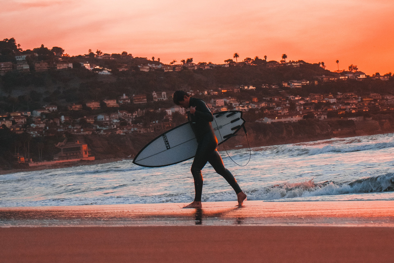 Surfer in a wetsuit walking away from the water on Los Angeles' Torrance Beach.