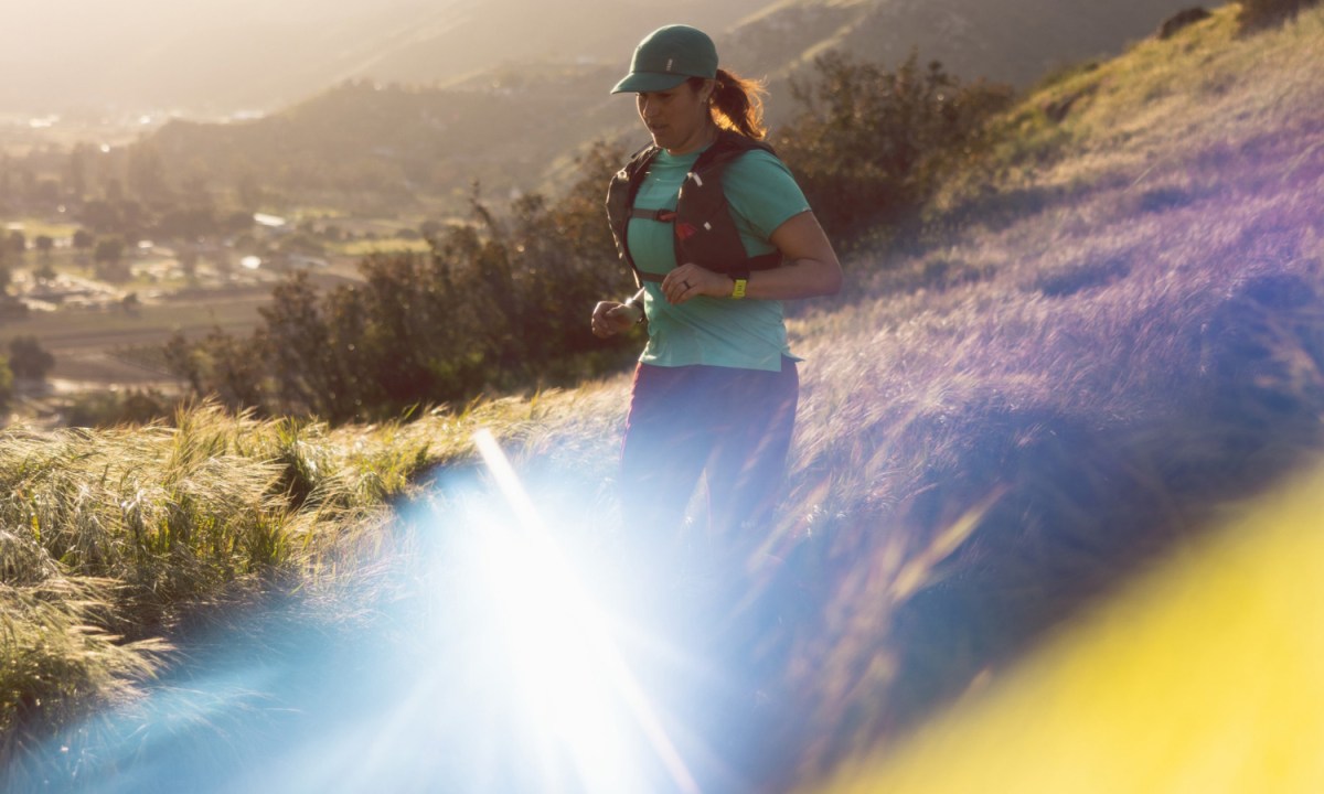 Woman trail running down a hill with houses in the background.