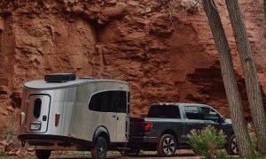 Black pickup truck towing an REI Co-op Special Edition Basecamp 20X travel trailer through a desert landscape.