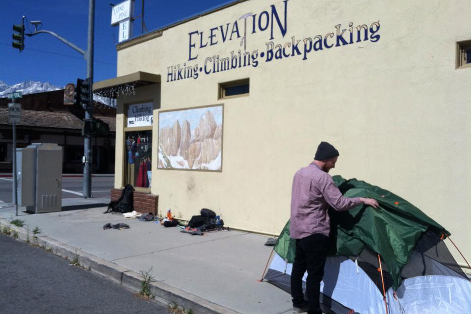 Man pitching a tent right outside Elevation outdoor gear store in Lone Pine, California.