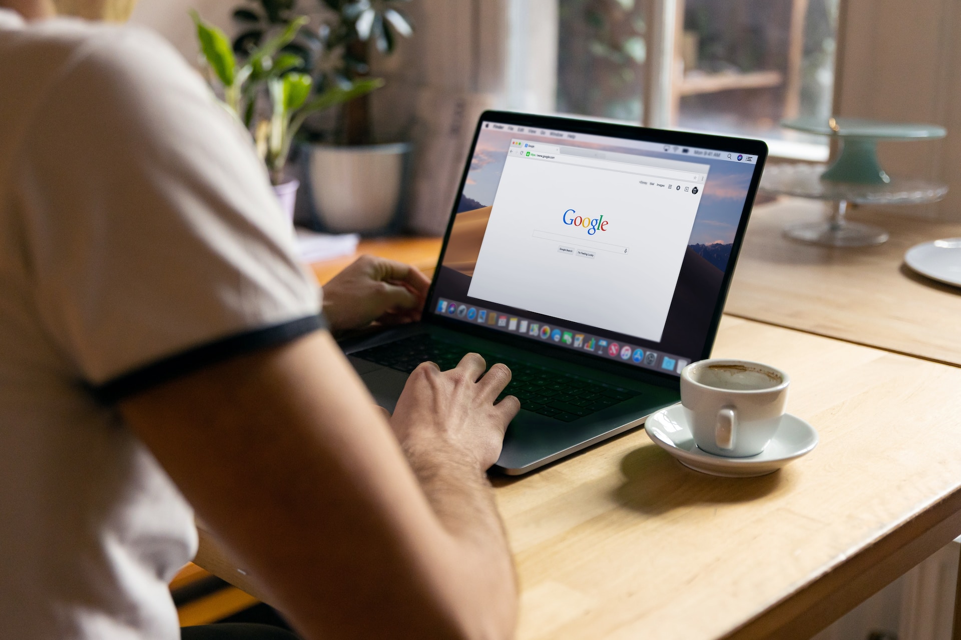 A man's shoulder and hands as he types on a laptop with a Google browser open