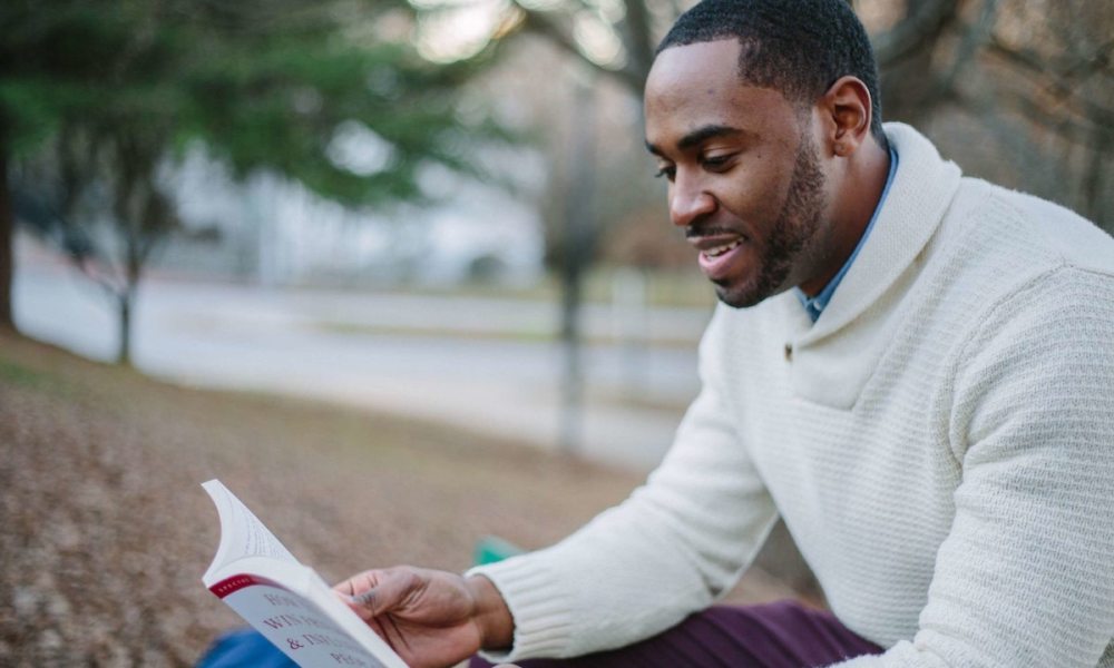 A man reading a book while sitting outside.