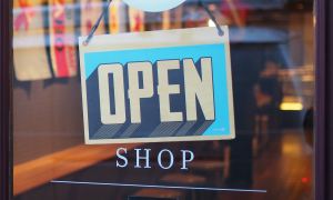 Gray and blue "OPEN" sign hanging on a the front door of a small shop.