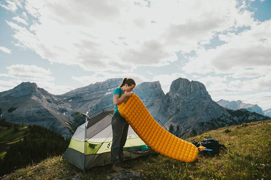 Young woman standing on a hill inflating a Nemo Tensor sleeping pad.