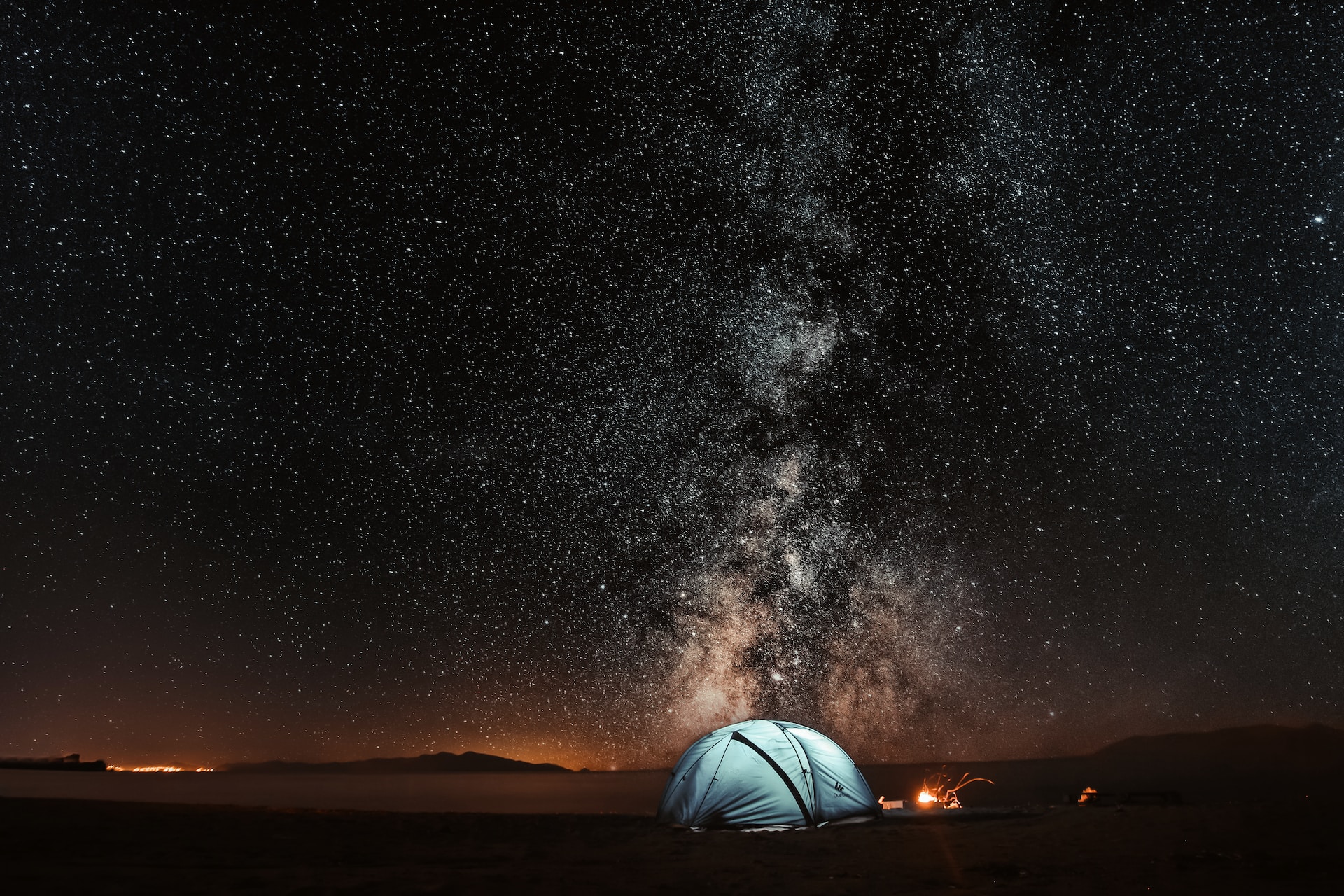 A single tent lit from the inside under a clear night sky with views of the Milky Way.