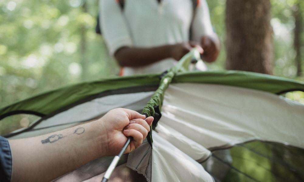 Closeup of two friends setting up a tent in the woods.