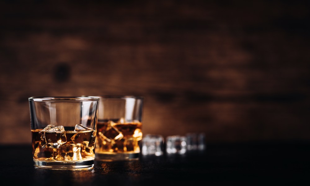 Whisky, whiskey, bourbon or cognac with ice cudes on black stone table and wood background