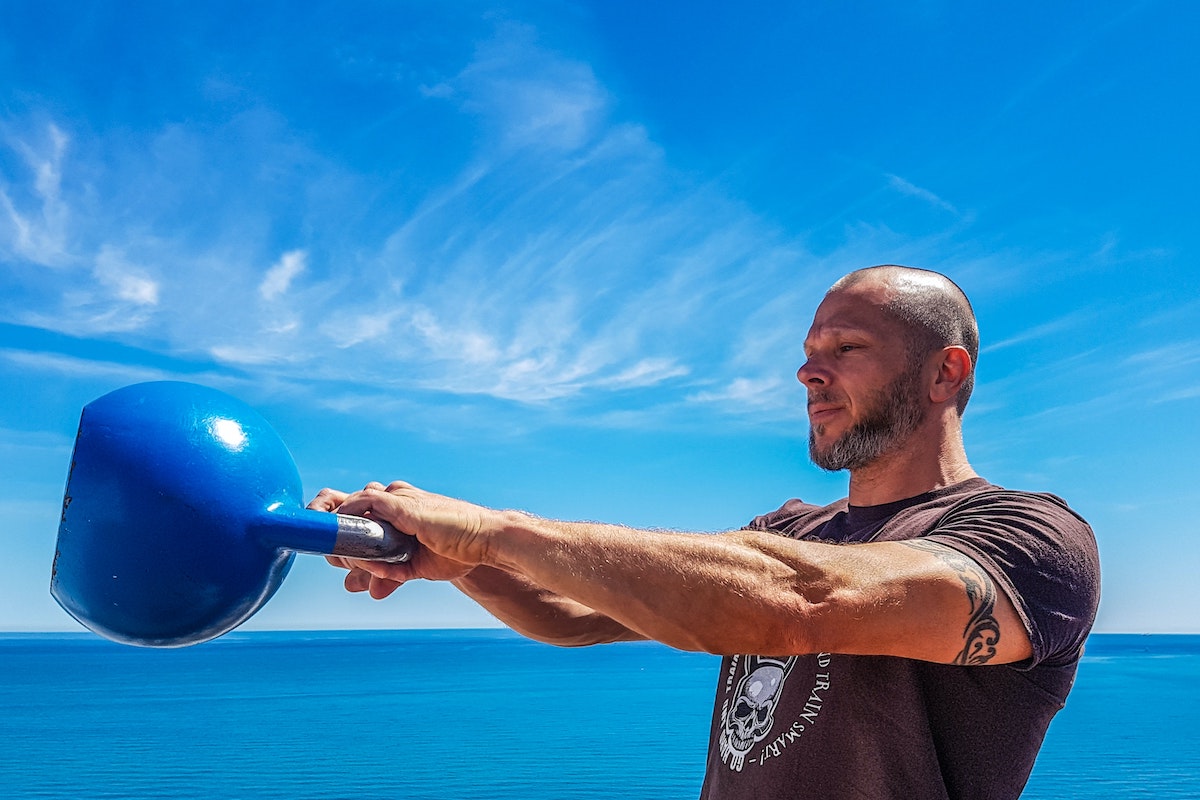 a man swinging a kettlebell by a blue sky