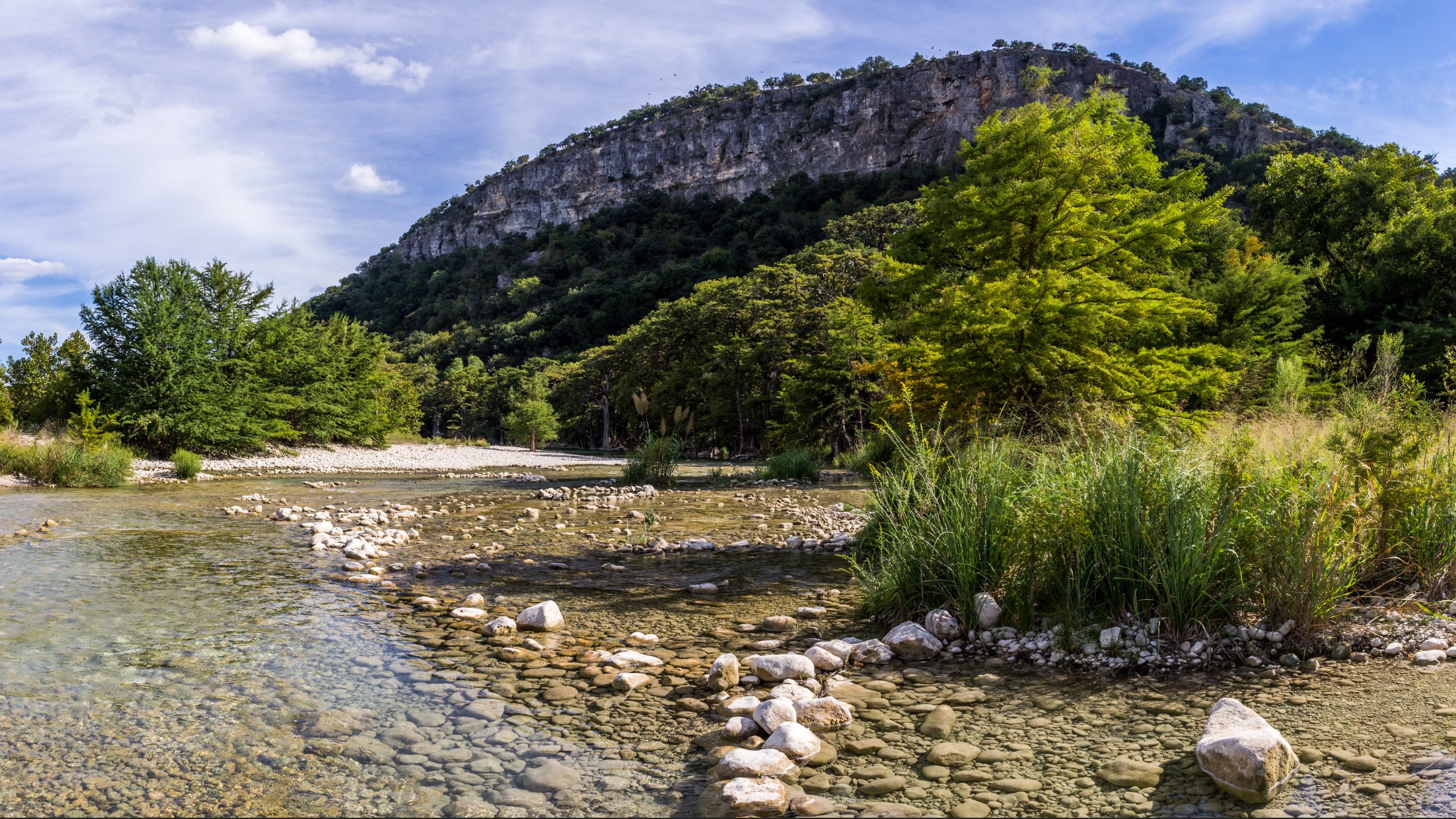 A shallow rocky bed of water with a view of Old Baldy mountain in Garner State Park