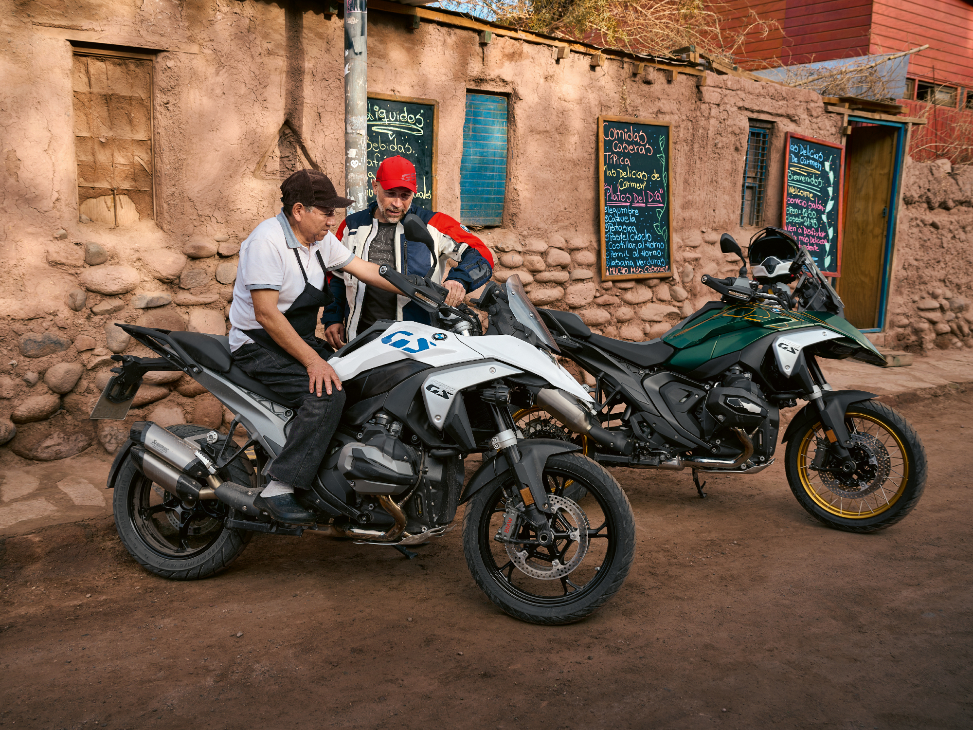 Two 2024 BMW R 1300 GS Adventure Touring Motorcycles Parked Outside A Cafe With A Cook Sitting On One As The Owner Looks On ?fit=800%2C599&p=1