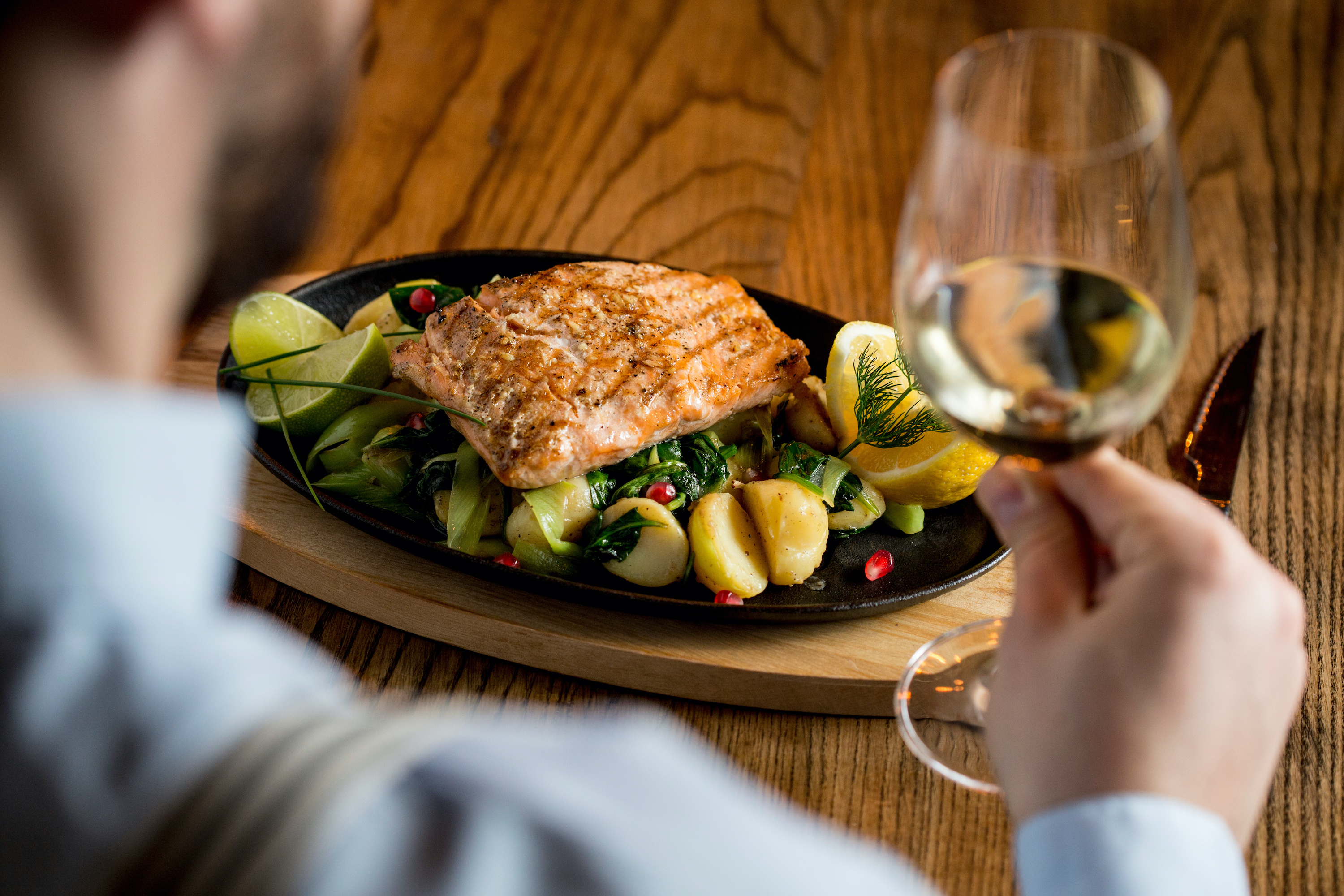 Young man eating salmon fillet with gratinated potatoes, leek and spinach in the restaurant with glass of white wine