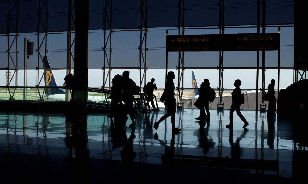 People walking through an airport with large windows in the background