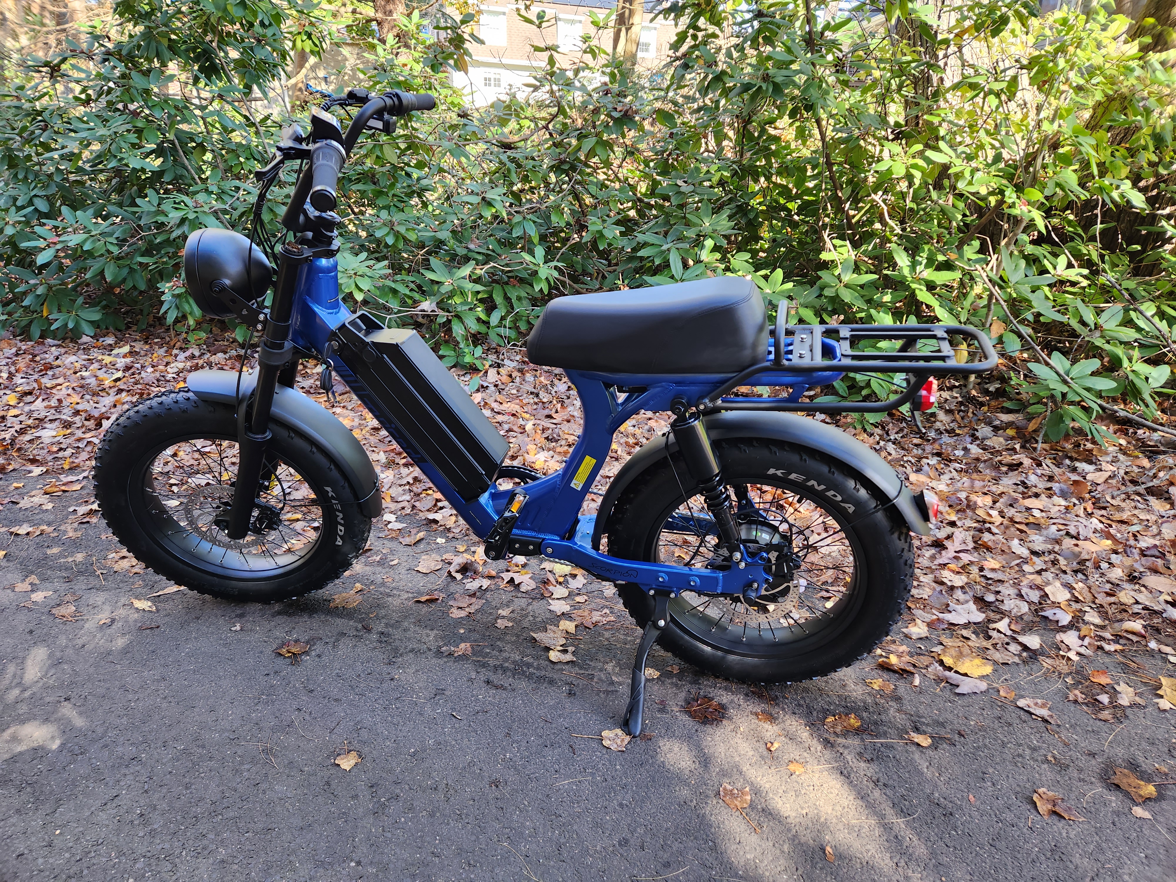 Juiced Bikes Scorpion X2 moped-style e-bike parked on asphalt with leaves and tress in the background