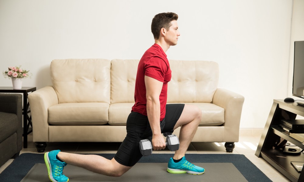 Profile view of a man lunge red shirt young and fit man doing kneeling lunges with a pair of dumbbells at home