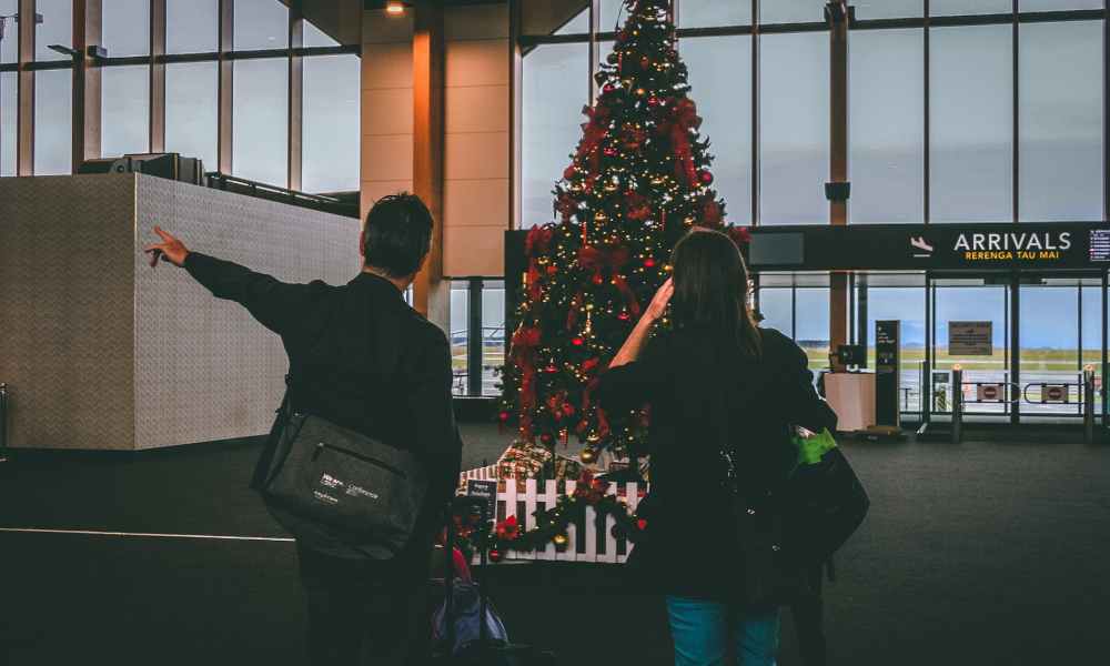 A man and woman inside of an airport stand in front of a christmas tree