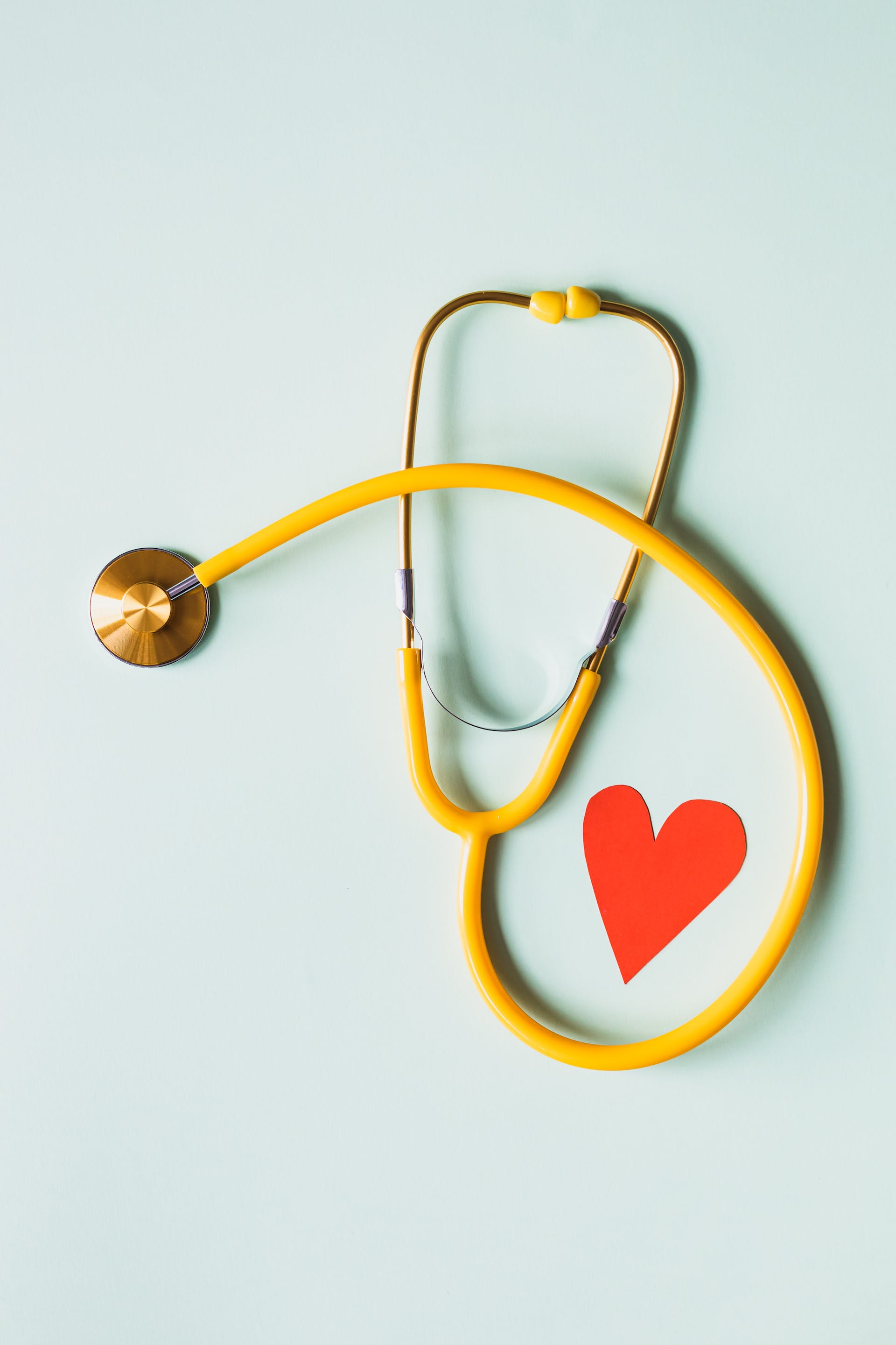 Stethoscope wrapped around a small paper red heart on a light blue background