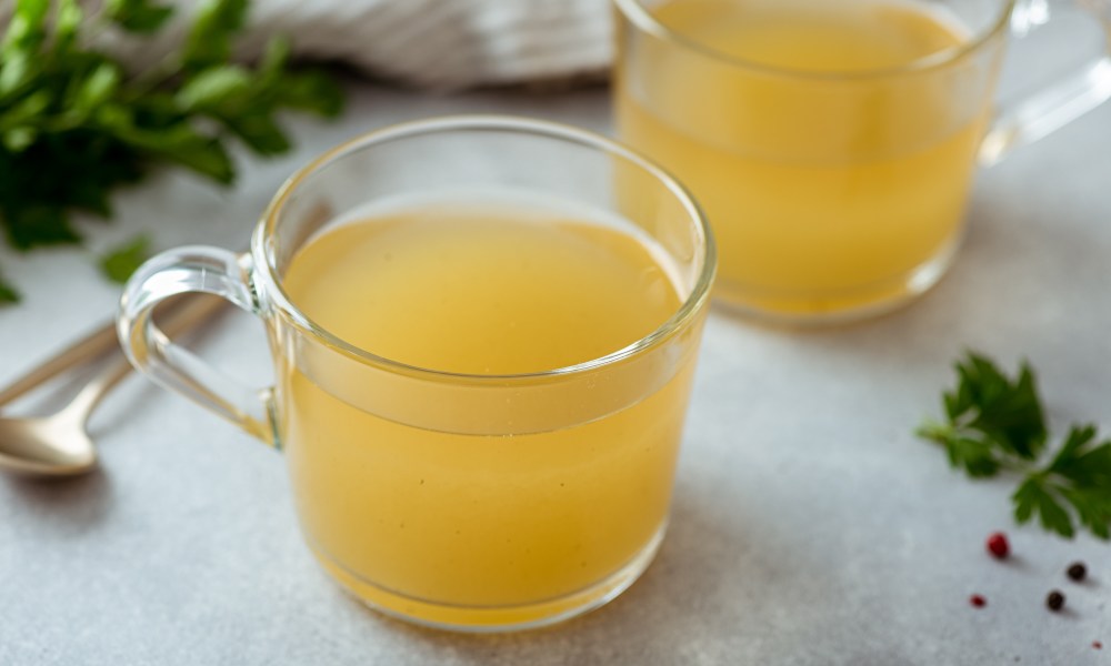 Bone broth in a glass cup on a light background, selective focus