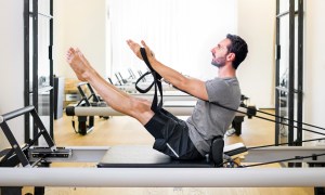 man doing pilates leg and arm stretch seated wooden floor