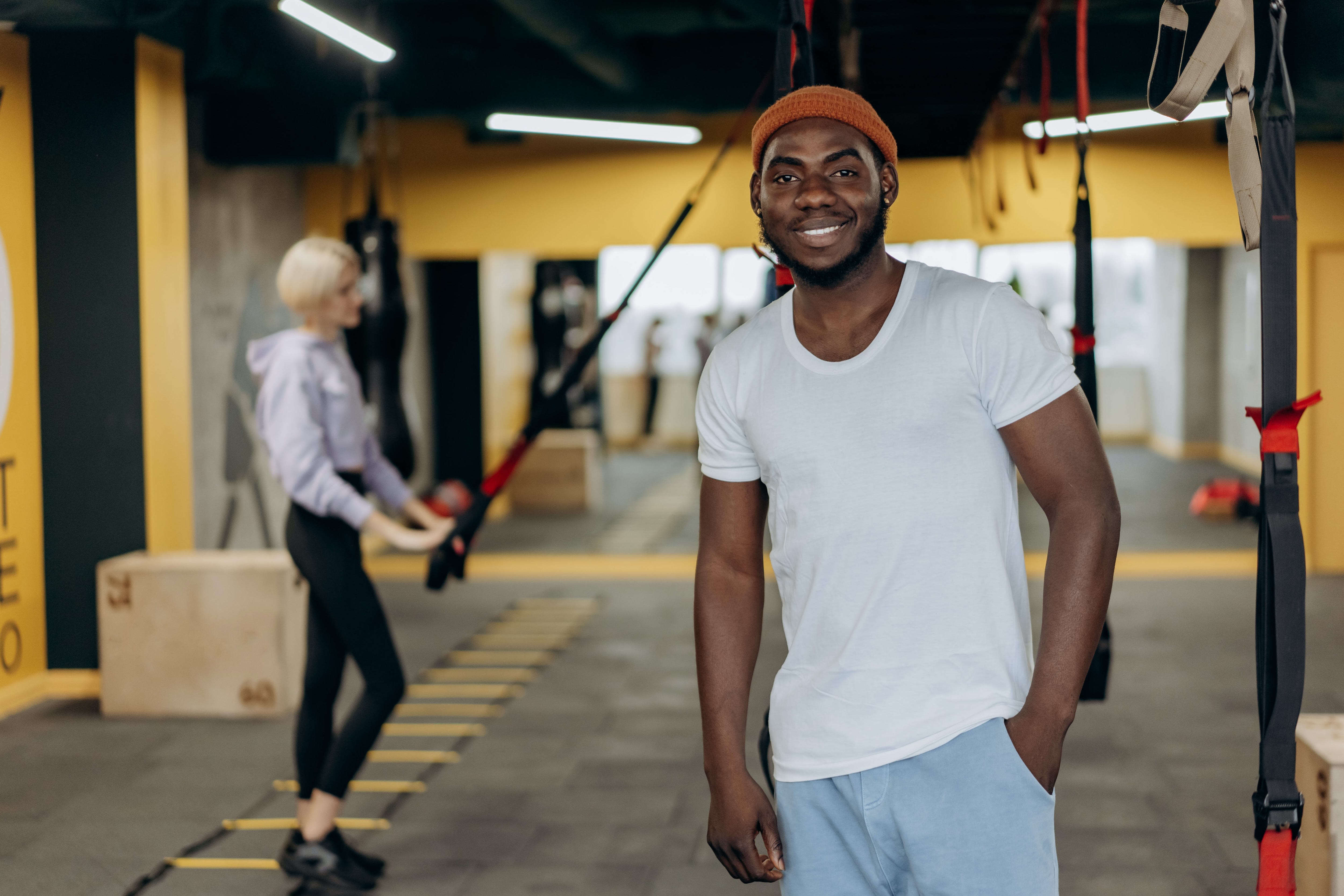 Man smiling at camera and woman working out behind him