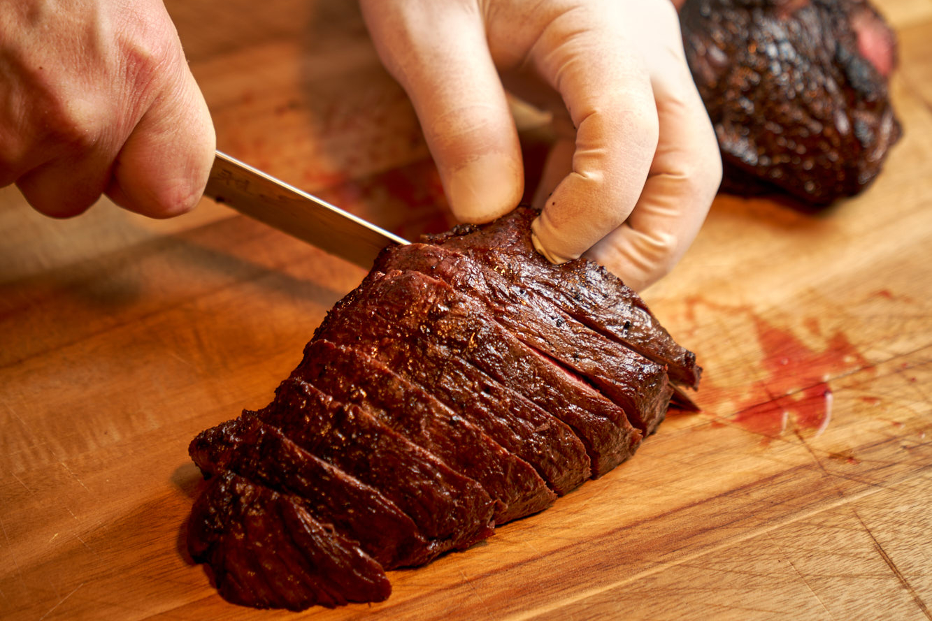 Hand slicing picanha steak on cutting board.