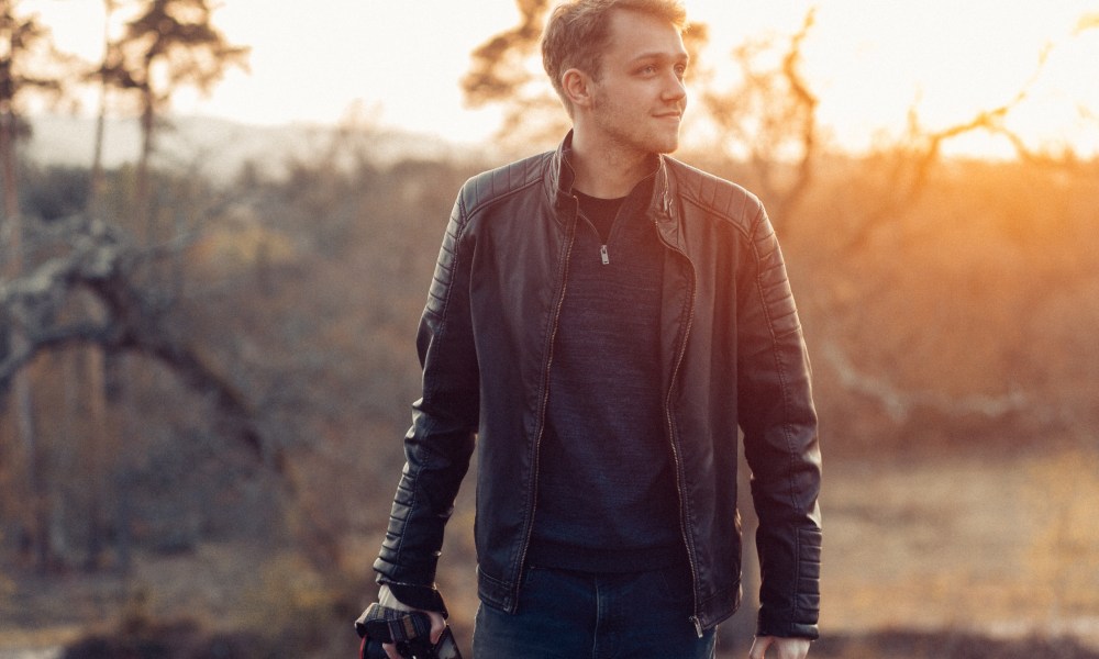 Man in leather jacket in woods with camera