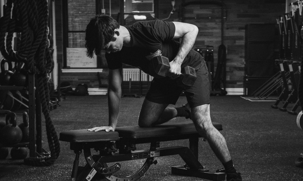 Man doing dumbbell rows on bench black and white pic