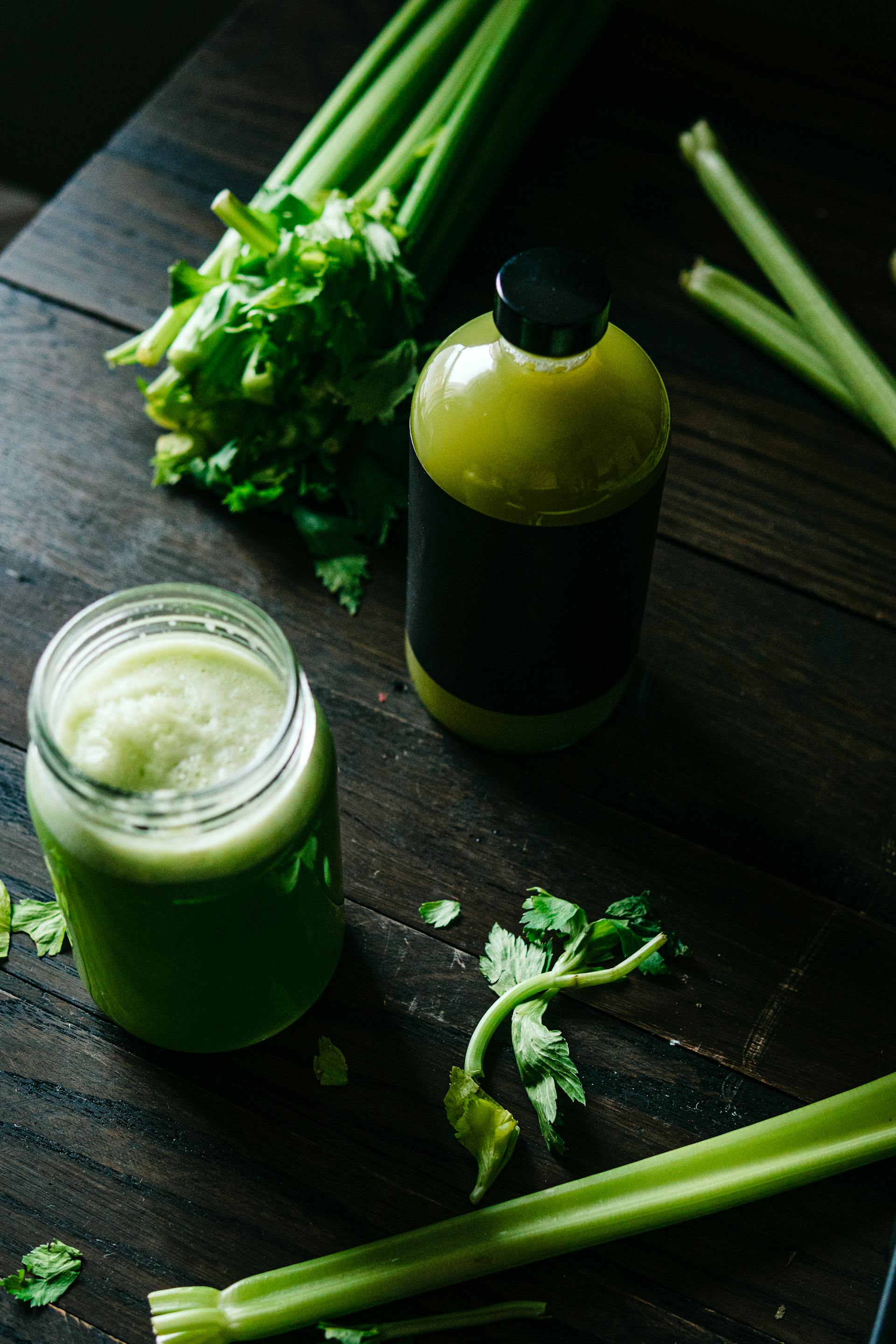 bottle of green drink celery juice on table with glass of green juice and celery stalks