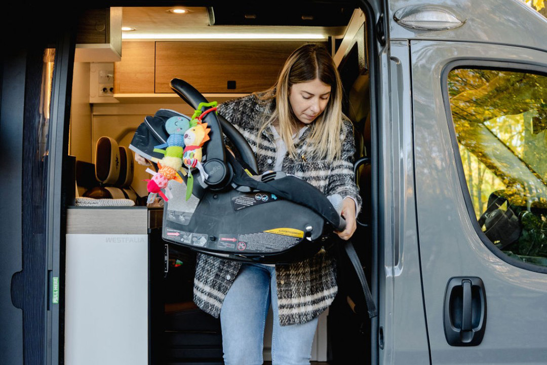 Young woman stepping out of a Westfalia Wave van with a baby carrier.