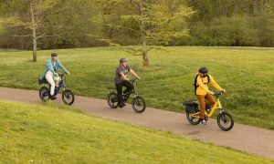 A group of people ride Co-op Cycles Generation e1.1 Electric Bikes through a park.