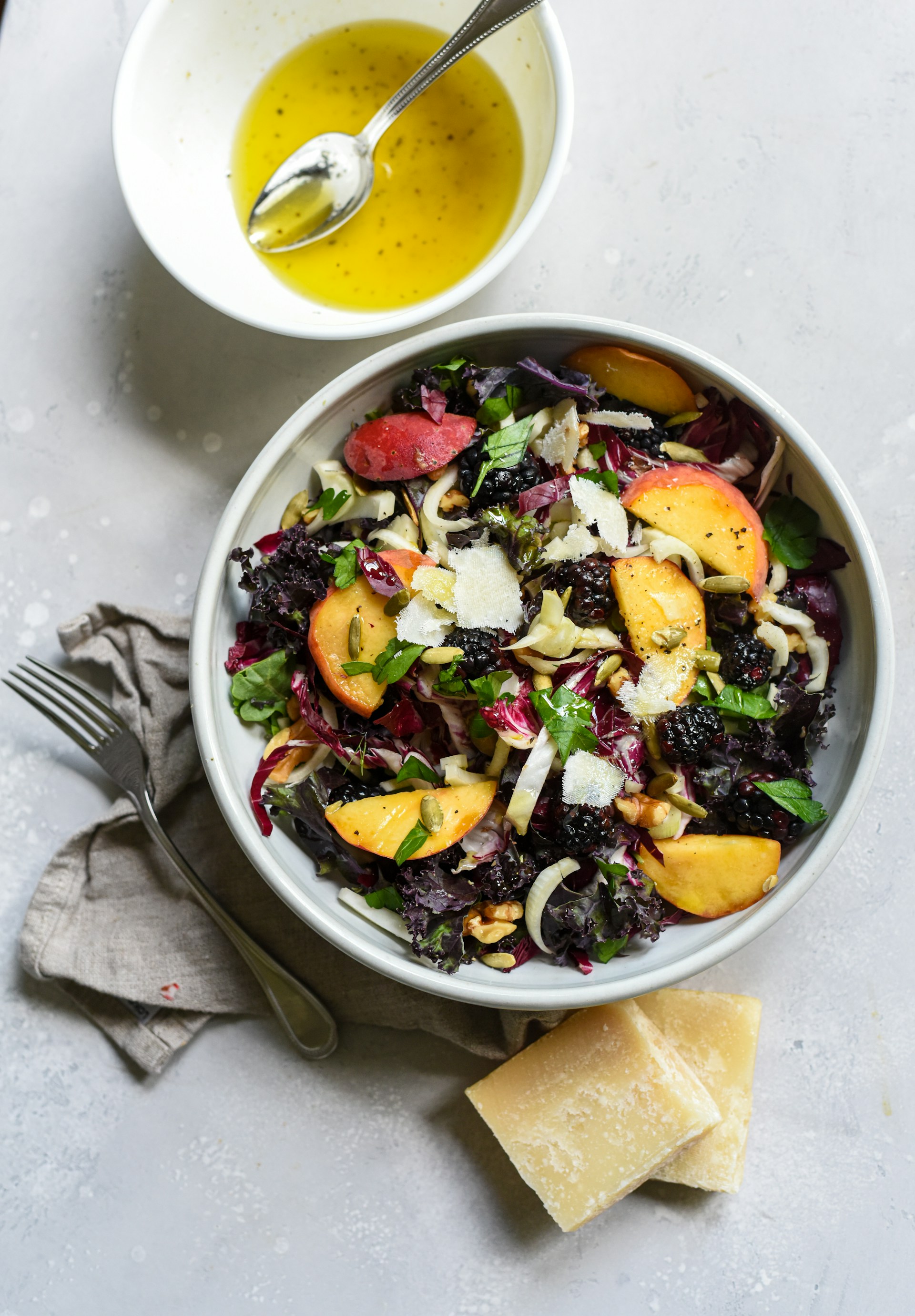 green salad with olive oil in a white bowl next to salad on white table