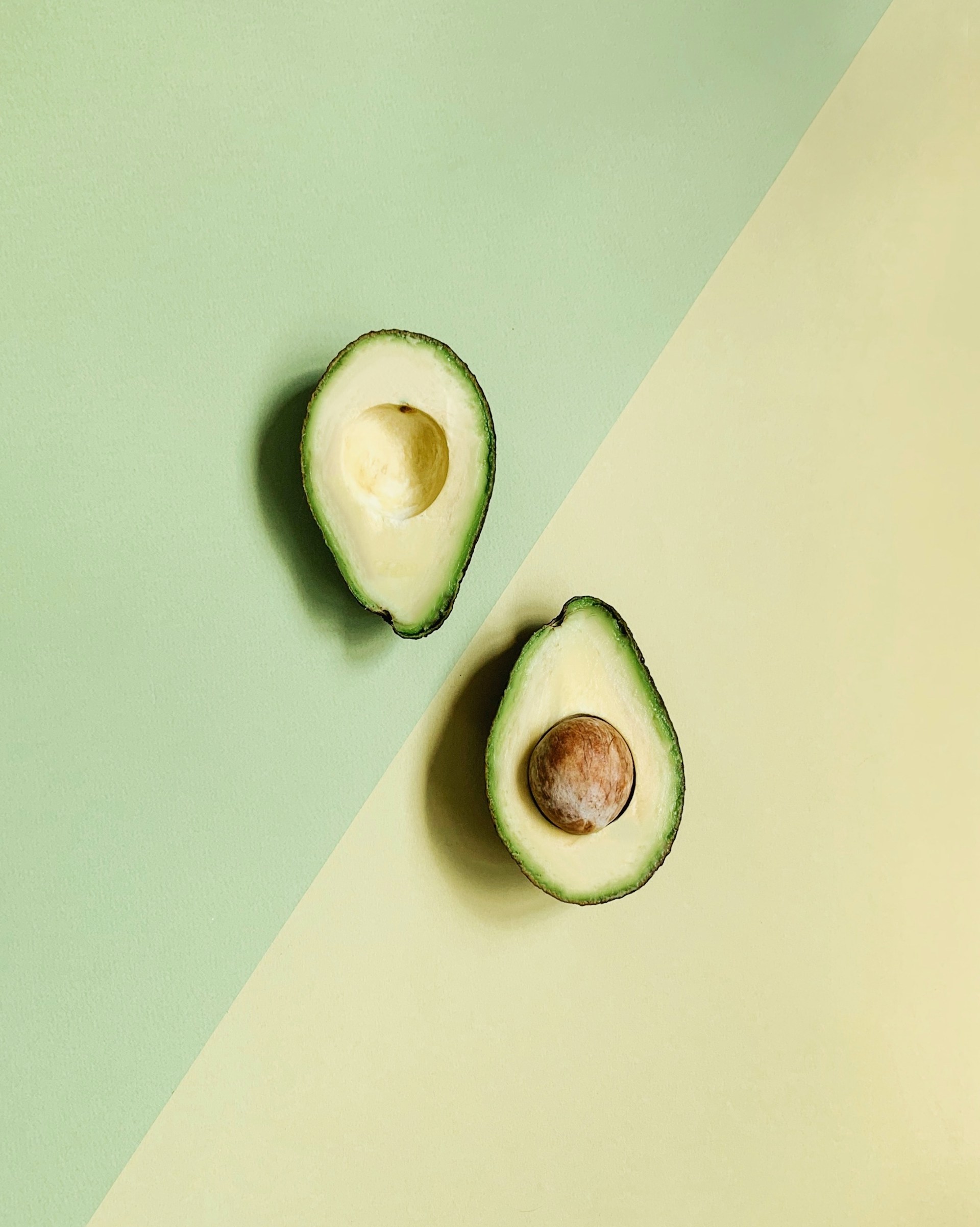 Avocado cut in half birds eye view on green and yellow background