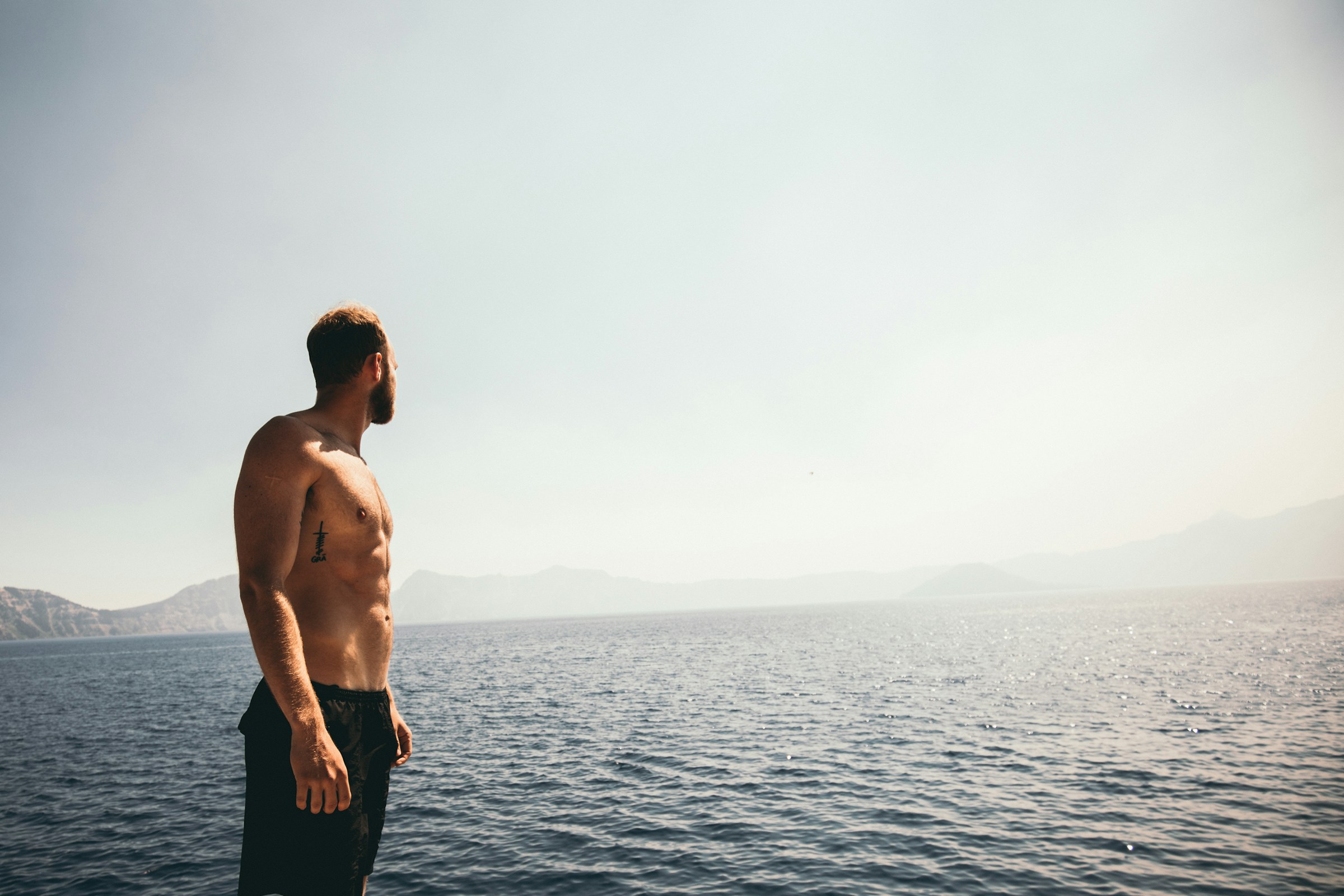 man shirt off with abs looking over ocean