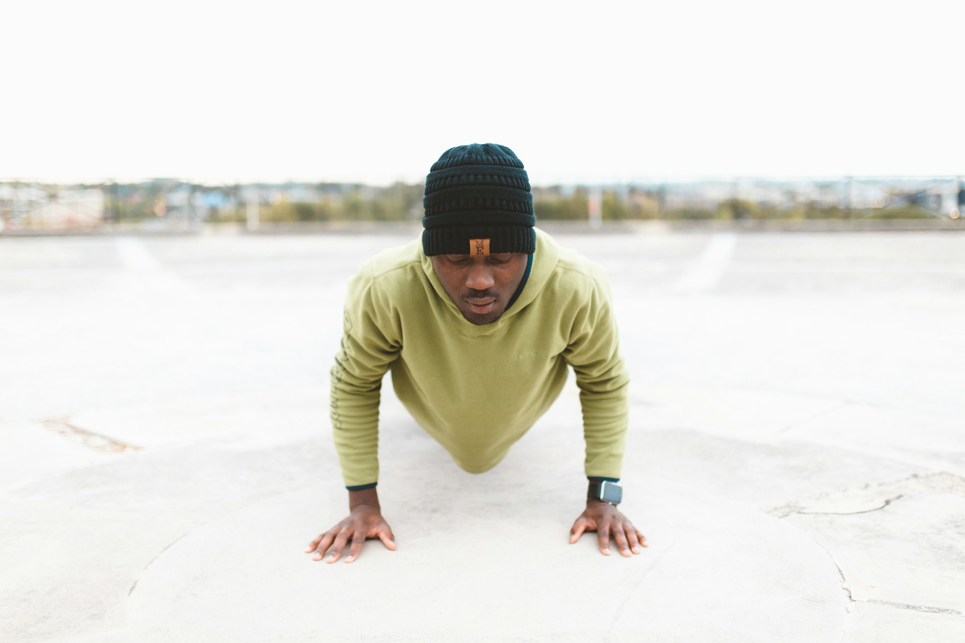 man wearing black hat and green shirt doing pushup or plank outside