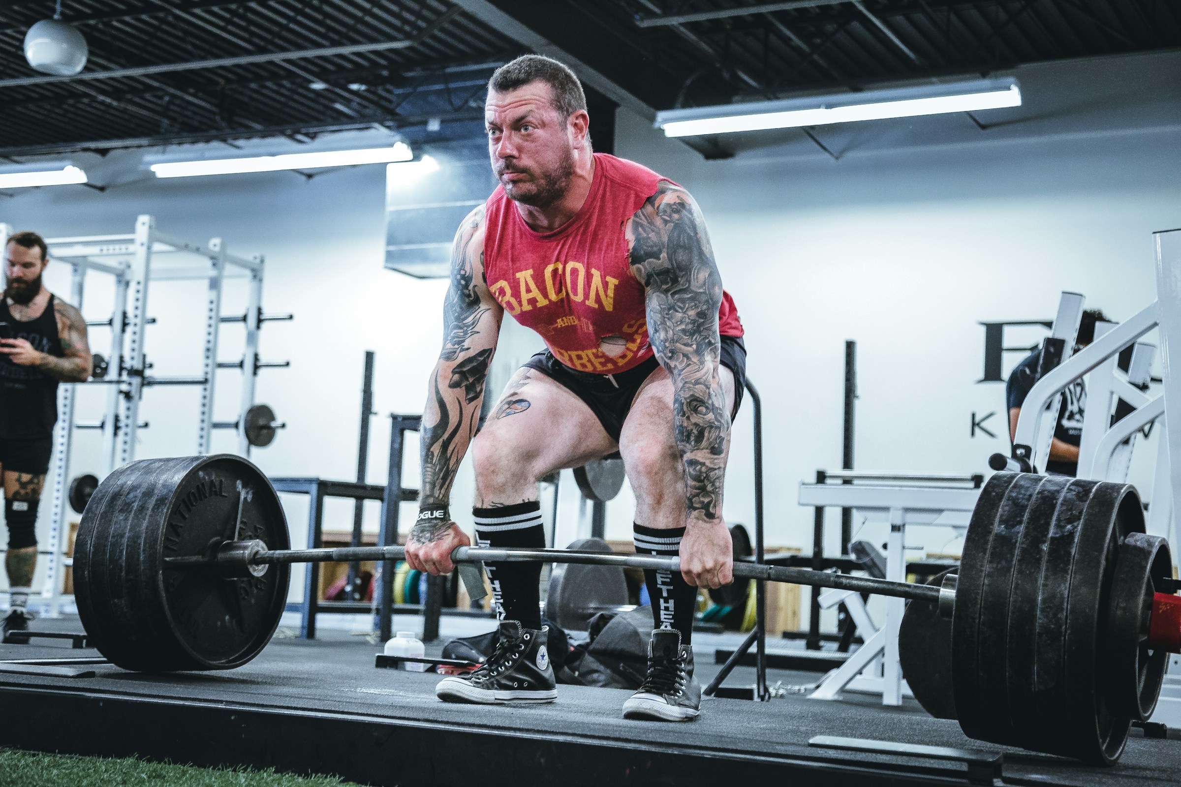 man wearing red shirt and shorts in gym weight lifting dead lift man with tattoos