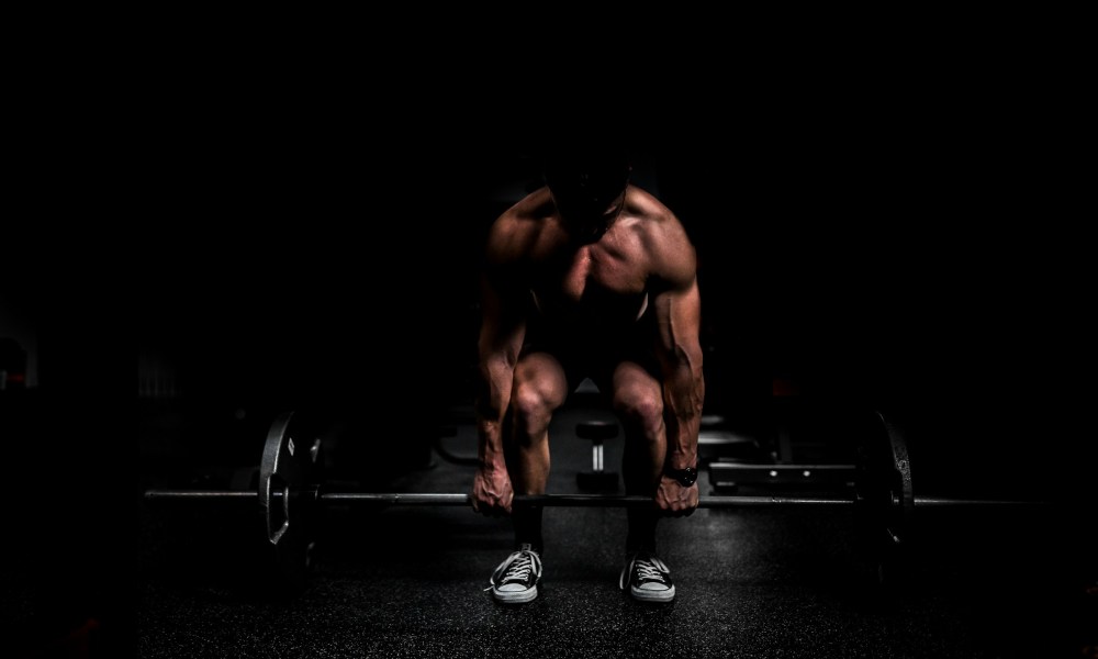 Shirtless man doing a deadlift weight lifting exercise with black background