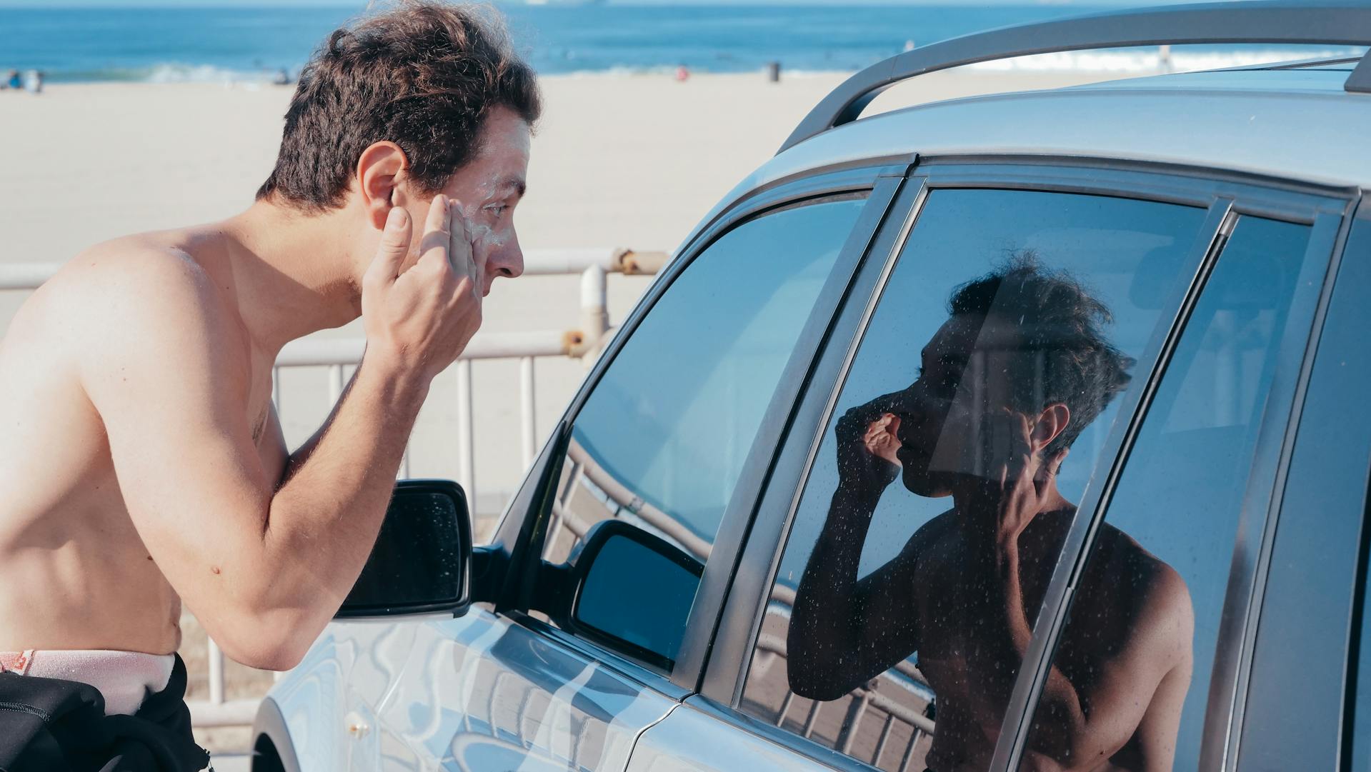 man applying sunscreen in front of car