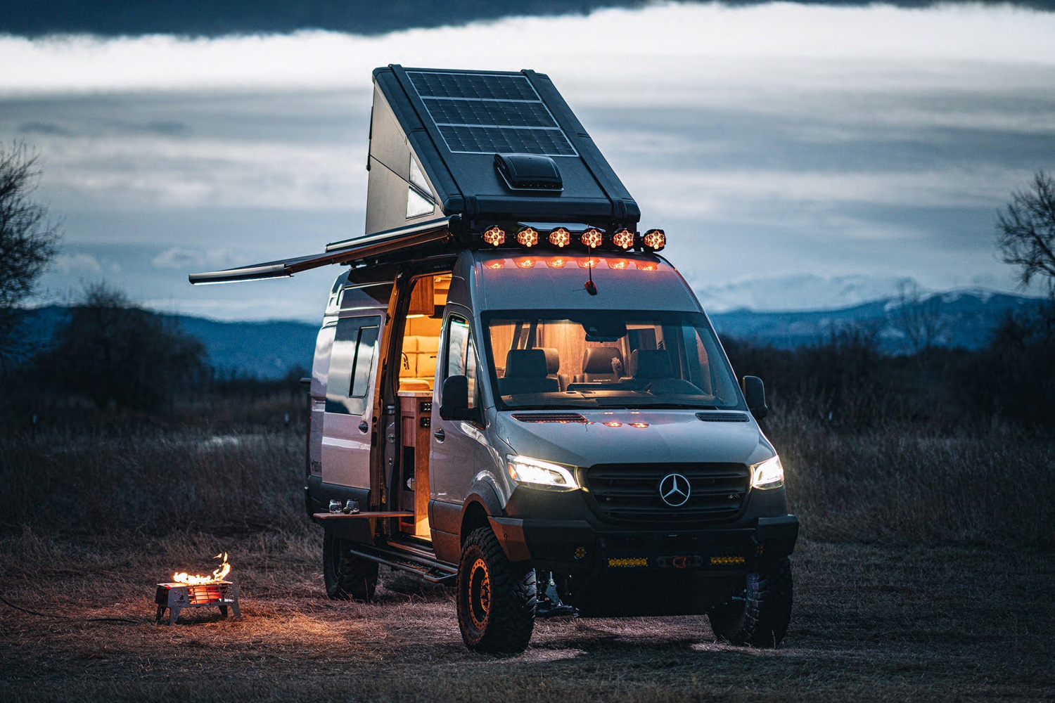 Redtail Overland's Skyloft camper van lit up at dusk in a field.