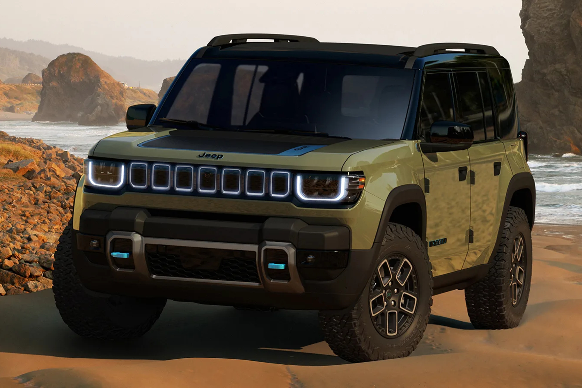 Green Jeep Recon Concept EV on beach with rocky hills nearby and in the background.